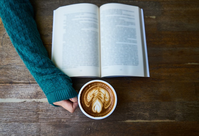 iemand leest een boek en heeft een kop koffie in de hand