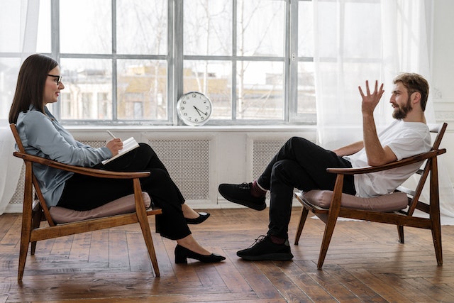 twee mensen zitten tegen over elkaar in een stoel en discussiëren met elkaar